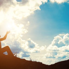 Silhouette of woman praying over beautiful sunrise background